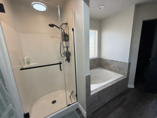 Walk-in shower with clear glass enclosure and black hardware, accompanied by a built-in jetted tub with tile surround