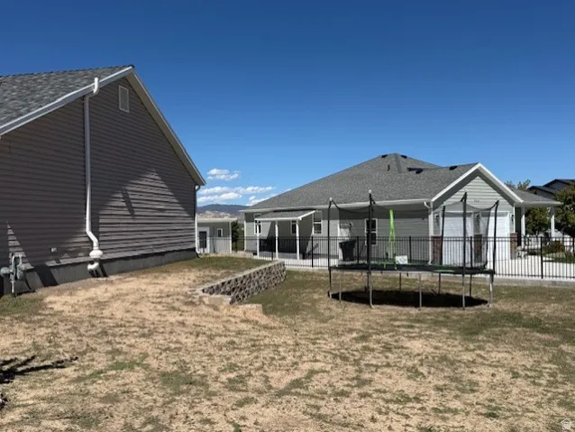 Siding exterior with a covered patio, black metal fencing, and a retaining wall