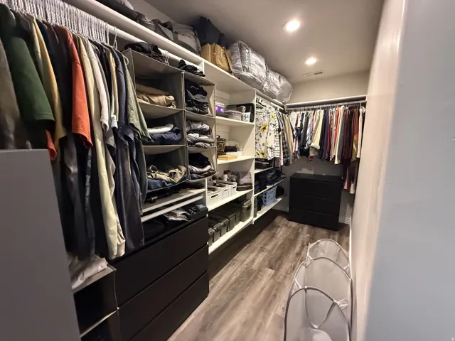 Walk-in closet featuring built-in shelving, multiple hanging rods, drawer storage, and wood-finish flooring