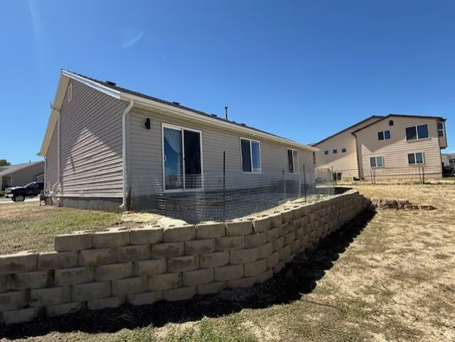 Rear exterior featuring light-toned horizontal siding, a sliding glass door, multiple windows, and a retaining wall constructed of stacked stone blocks
