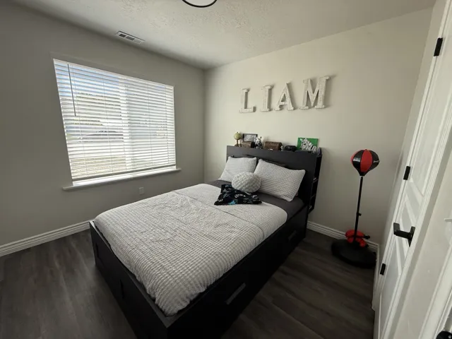 Wood-finish flooring with white trim, a single window with blinds, and white panel doors with black hardware