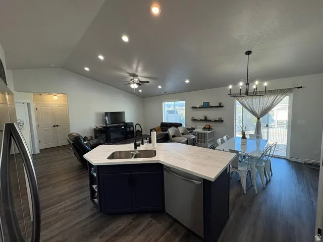 Vaulted ceilings with recessed lighting, wood-finish flooring, kitchen island with built-in sink, stainless steel dishwasher, and sliding glass door