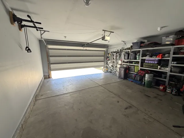Concrete flooring garage with an automatic roll-up door, overhead lighting, and built-in wall shelving