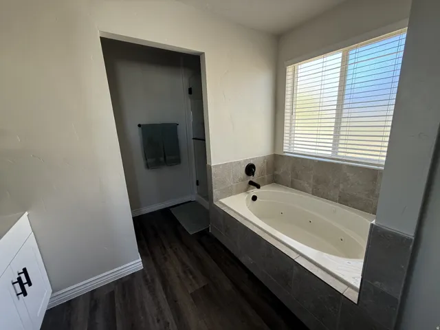 Built-in jetted tub with matte black fixtures, surrounded by grey tile and a window with blinds
