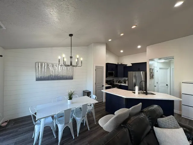 Open-concept living space featuring wood-finish flooring, a contemporary black chandelier, a white shiplap accent wall, a kitchen island with a light-toned countertop, and dark blue cabinetry