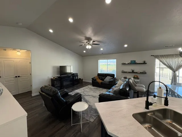 Vaulted ceiling with recessed lighting, wood-finish flooring, built-in floating shelves, large windows, and a stainless steel double basin sink with a matte black faucet