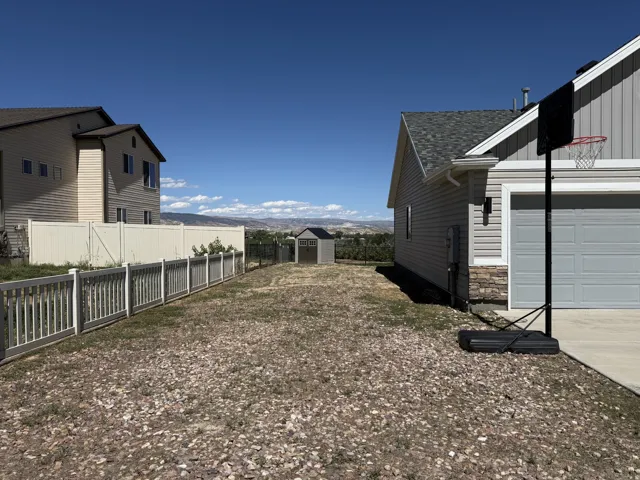 Expansive backyard with a storage shed, white privacy fencing, and distant mountain scenery