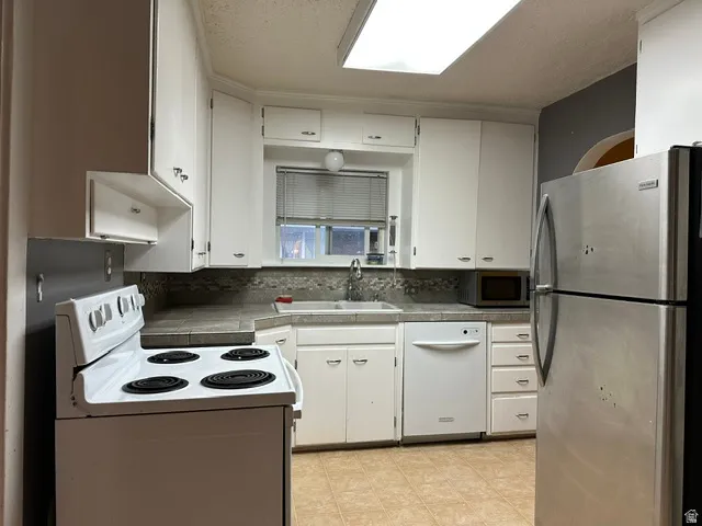 Kitchen featuring white cabinetry, a built-in dishwasher, stainless steel refrigerator, and an electric range