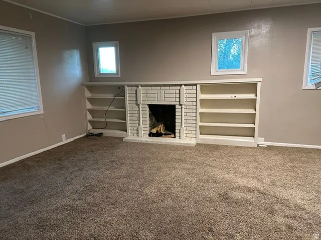 Carpeted room featuring a fireplace with a white brick surround, mantel, and hearth, flanked by built-in shelving units