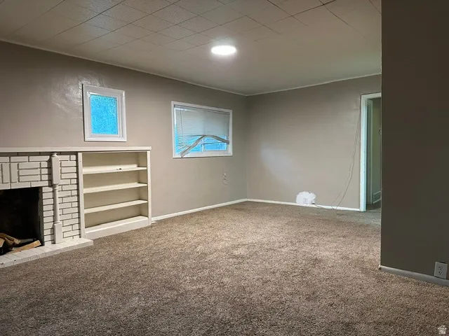 Brick-surround fireplace with hearth, built-in shelving, and carpeted flooring