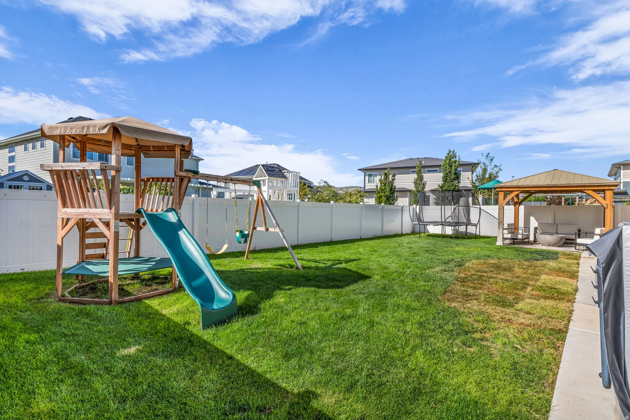 Expansive fenced yard featuring a wood playset with slide and swings, a wooden gazebo, and a concrete patio