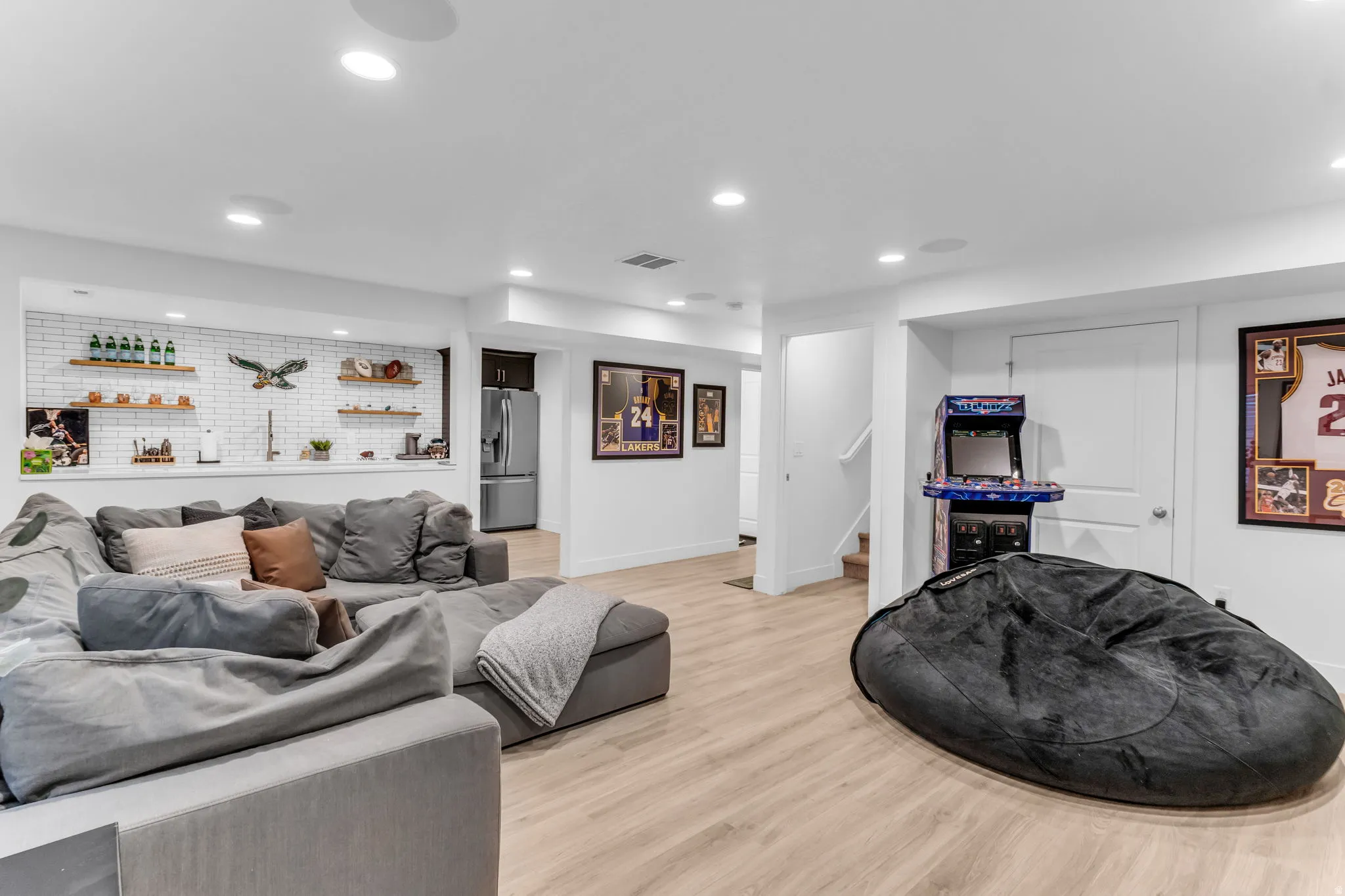 Recessed lighting, wood-finish flooring, built-in shelving, white subway tile accent wall, and a stainless steel refrigerator