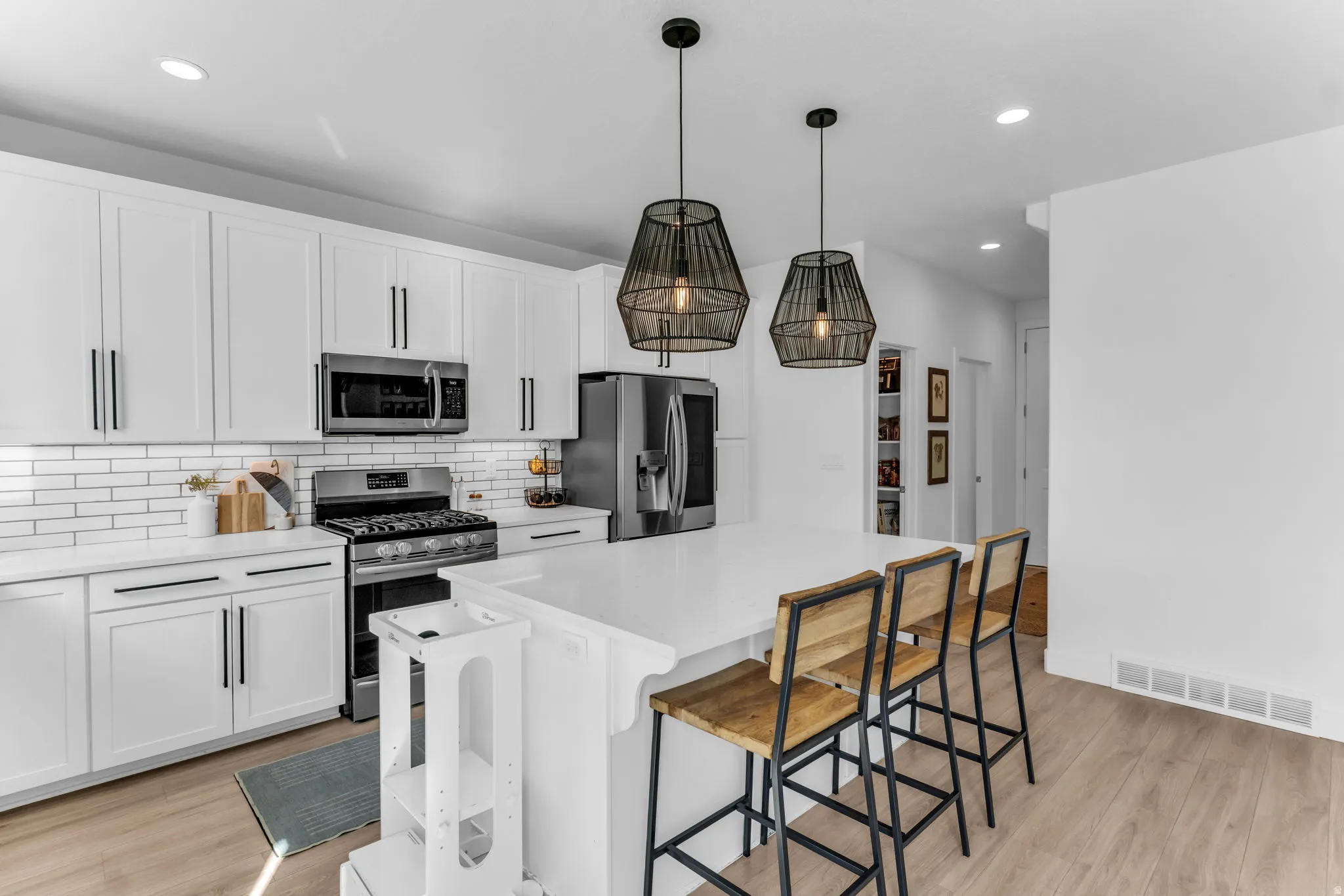 White shaker cabinetry, stainless steel appliances, white subway tile backsplash, white countertop island, and wood-finish flooring