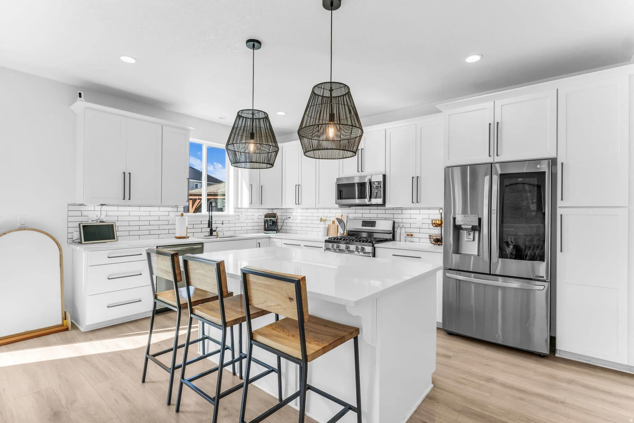 White cabinetry with modern hardware, stainless steel appliances, a center island with countertop seating, wood-finish flooring, and subway tile backsplash