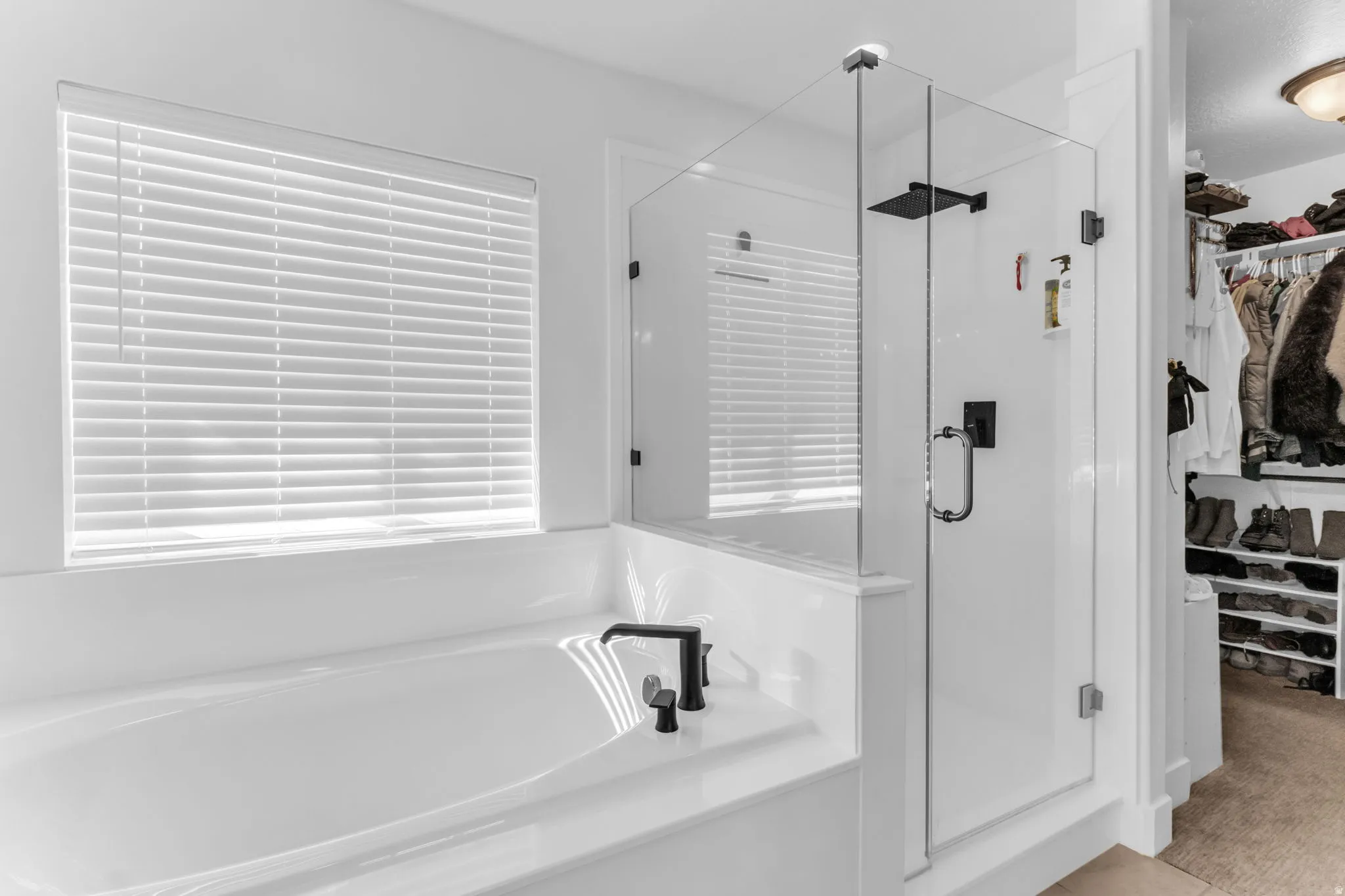 Freestanding soaking tub with matte black fixtures, glass-enclosed shower with matte black fixtures, and a custom closet system with ample storage