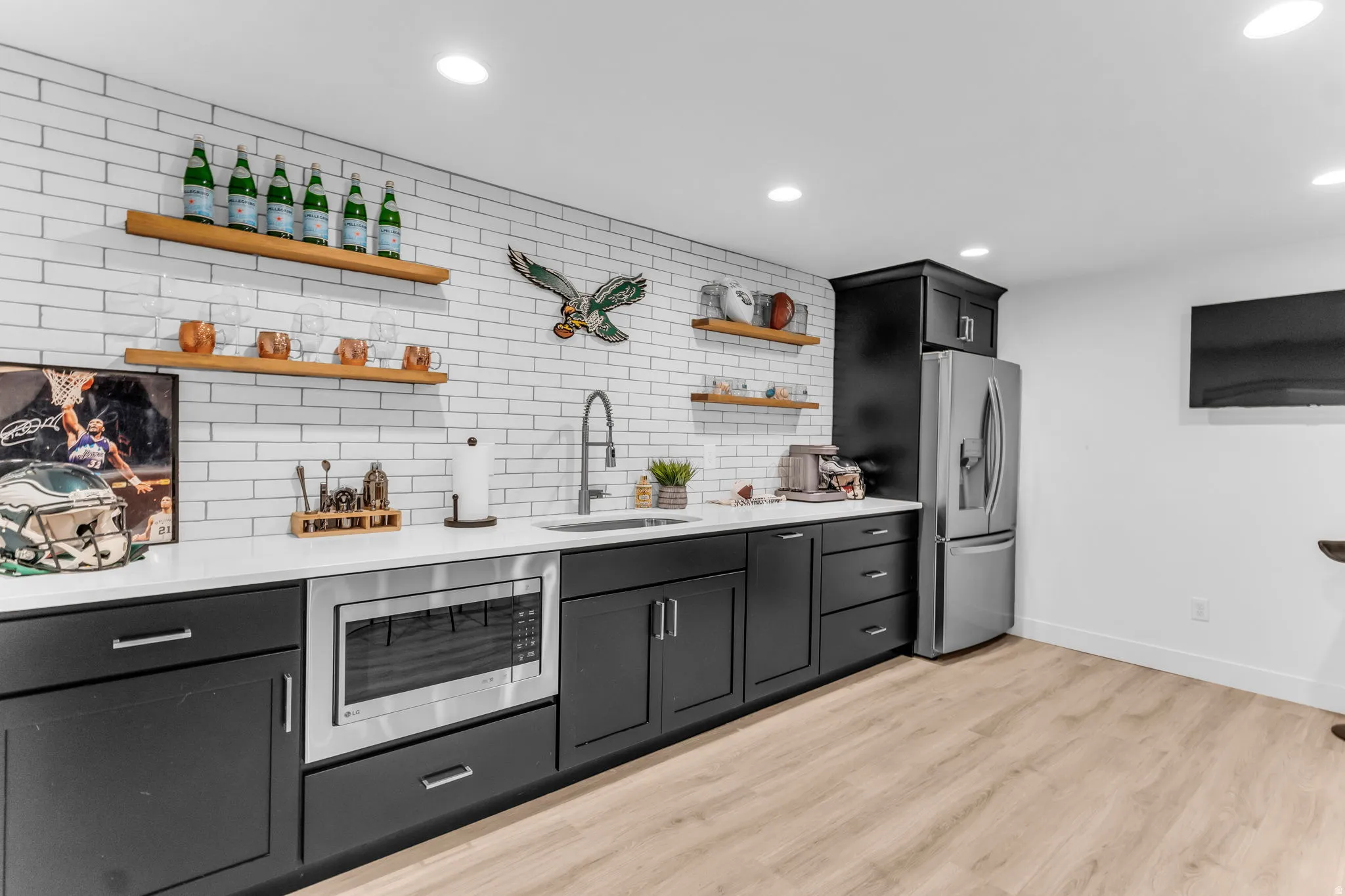 White subway tile backsplash, light wood-finish flooring, recessed lighting, matte black cabinetry, and stainless steel appliances
