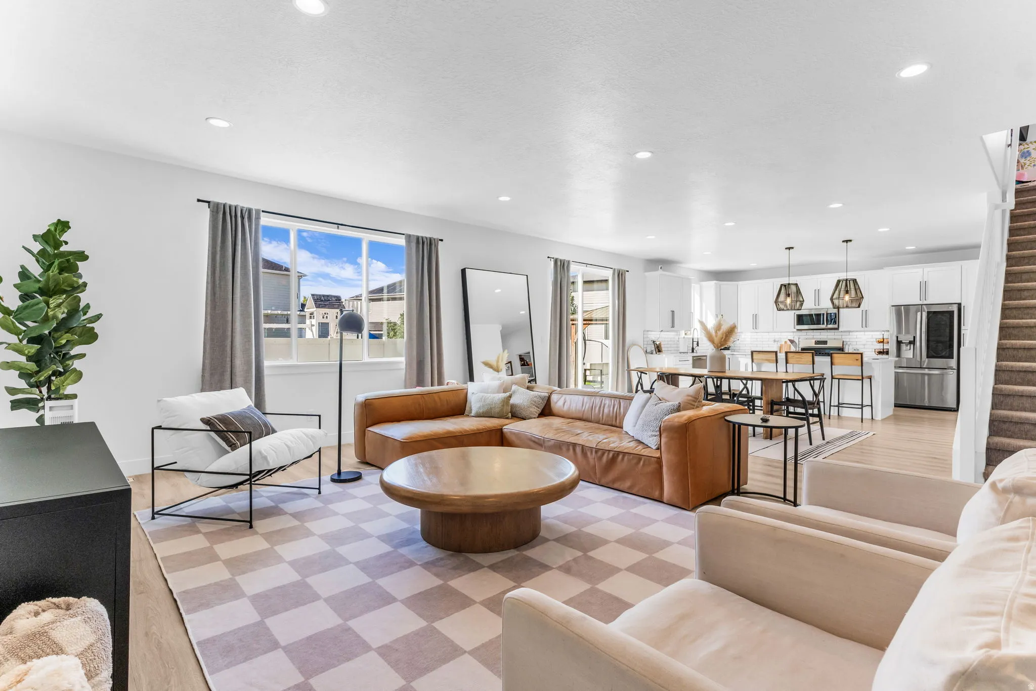 Recessed lighting, wood-finish flooring, white walls, and a visible kitchen with stainless steel appliances and pendant lighting