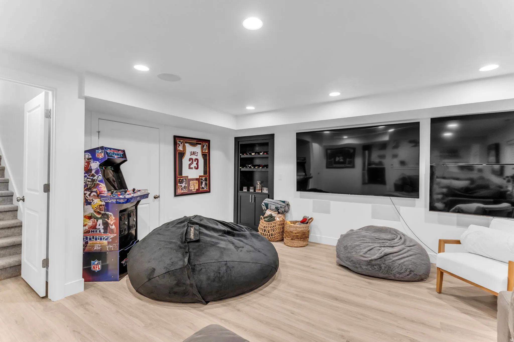 Recessed lighting, wood-finish flooring, built-in cabinetry, dual wall-mounted screens, and a staircase with carpeted treads