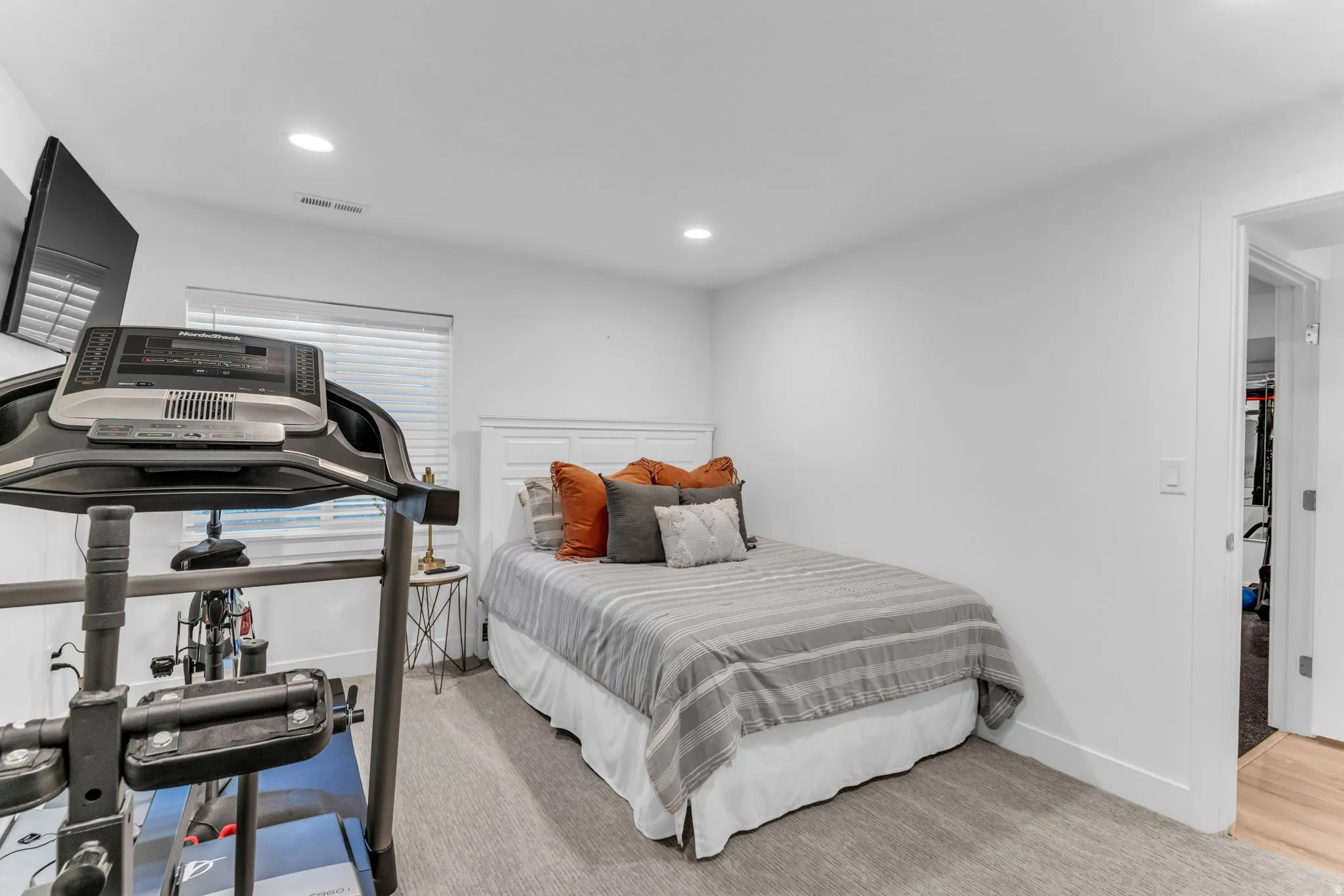 Recessed lighting, wood-finish flooring, white walls, and a white paneled headboard