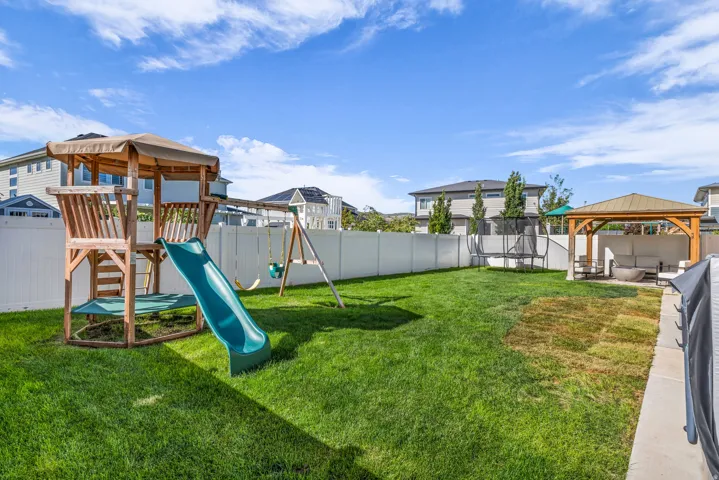 Expansive fenced yard featuring a wood playset with slide and swings, a wooden gazebo, and a concrete patio