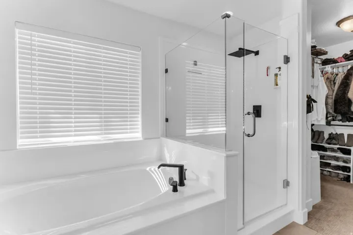 Freestanding soaking tub with matte black fixtures, glass-enclosed shower with matte black fixtures, and a custom closet system with ample storage