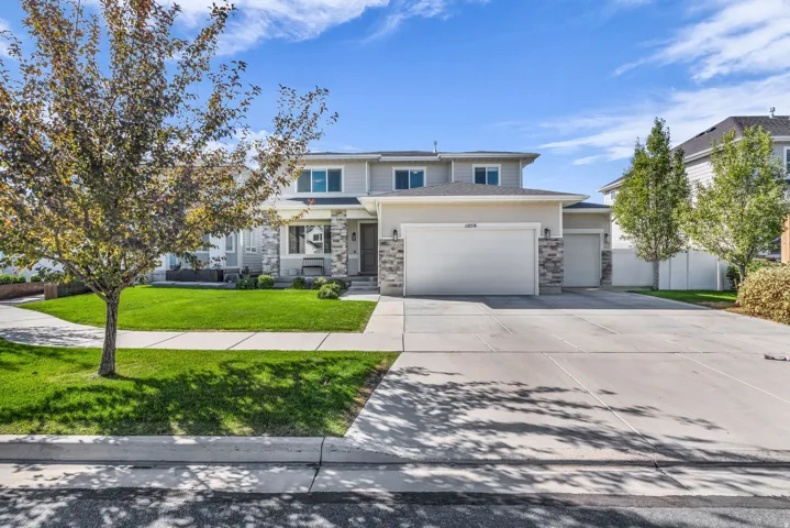 Two-story residence featuring a light-toned exterior, stone facade accents, and a dual-bay garage
