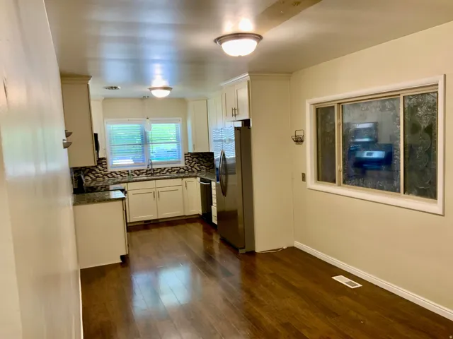 Kitchen featuring white cabinetry, wood-finish flooring, a mosaic tile backsplash, and a double-basin sink under a window