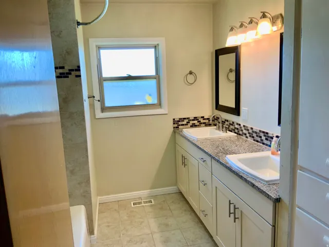 Dual vanity with granite-style countertop, white cabinetry, integrated sinks, and tiled backsplash