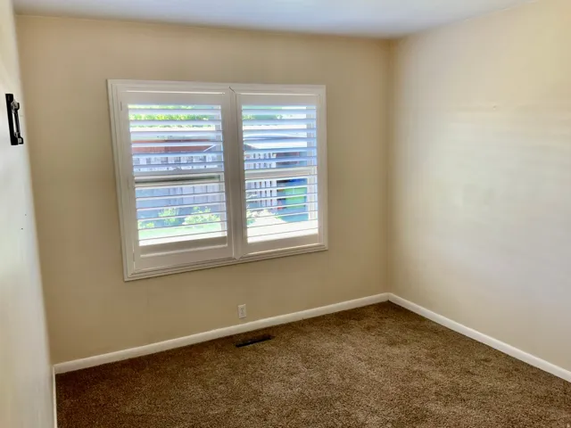 Window with white plantation shutters, neutral tone walls, and brown carpet
