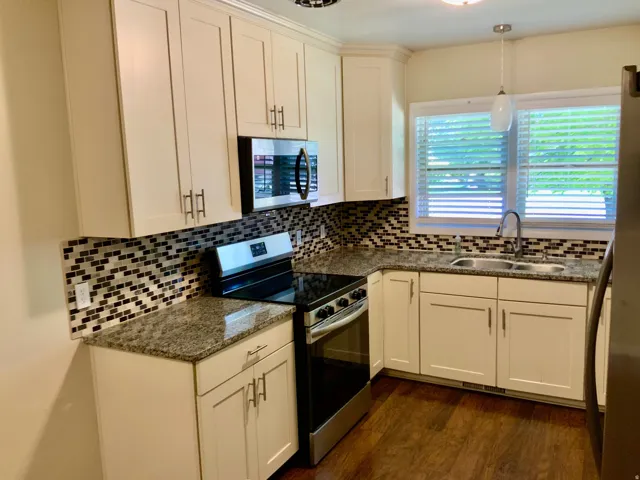 White shaker-style cabinetry with matte hardware, mosaic tile backsplash, granite countertops, and stainless steel appliances