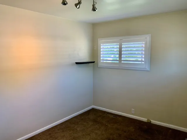 Window with white louvered shutters, track lighting with three fixtures, and a wall-mounted shelf