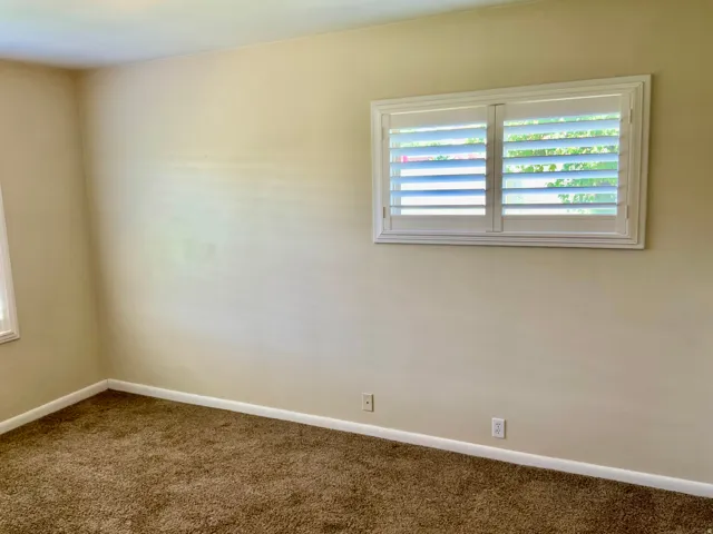 Window with white plantation shutters, neutral tone walls, and brown carpeting