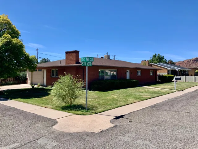 Brick exterior residence with an attached garage, featuring a paved driveway and a corner lot location with mature landscaping