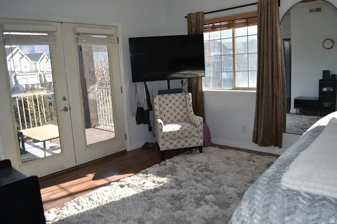 Hardwood-finish flooring, white double French doors, large window with blinds and drapes, wall-mounted television