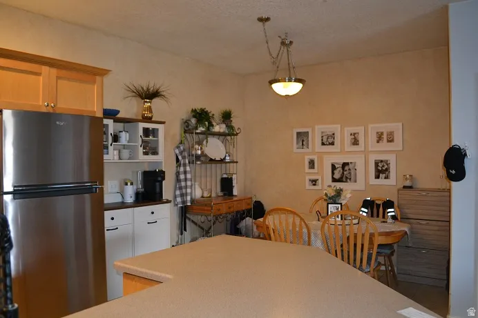 Stainless steel refrigerator, light wood-finish cabinetry, built-in white hutch, pendant lighting, and a neutral countertop