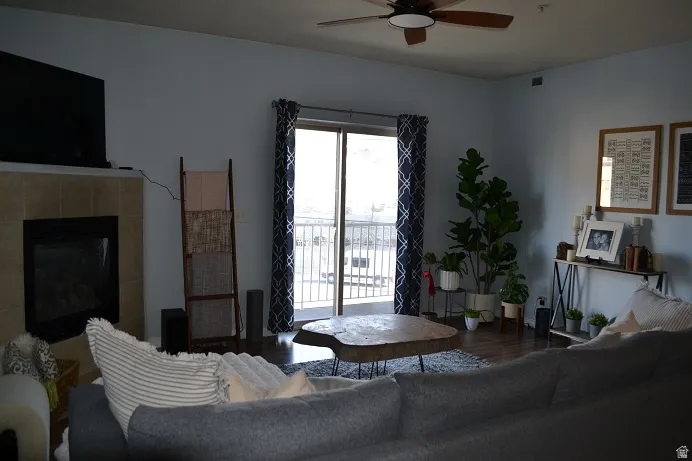 Recessed fireplace with tile surround, wood-finish flooring, ceiling fan with integrated lighting, and a sliding glass door providing exterior access