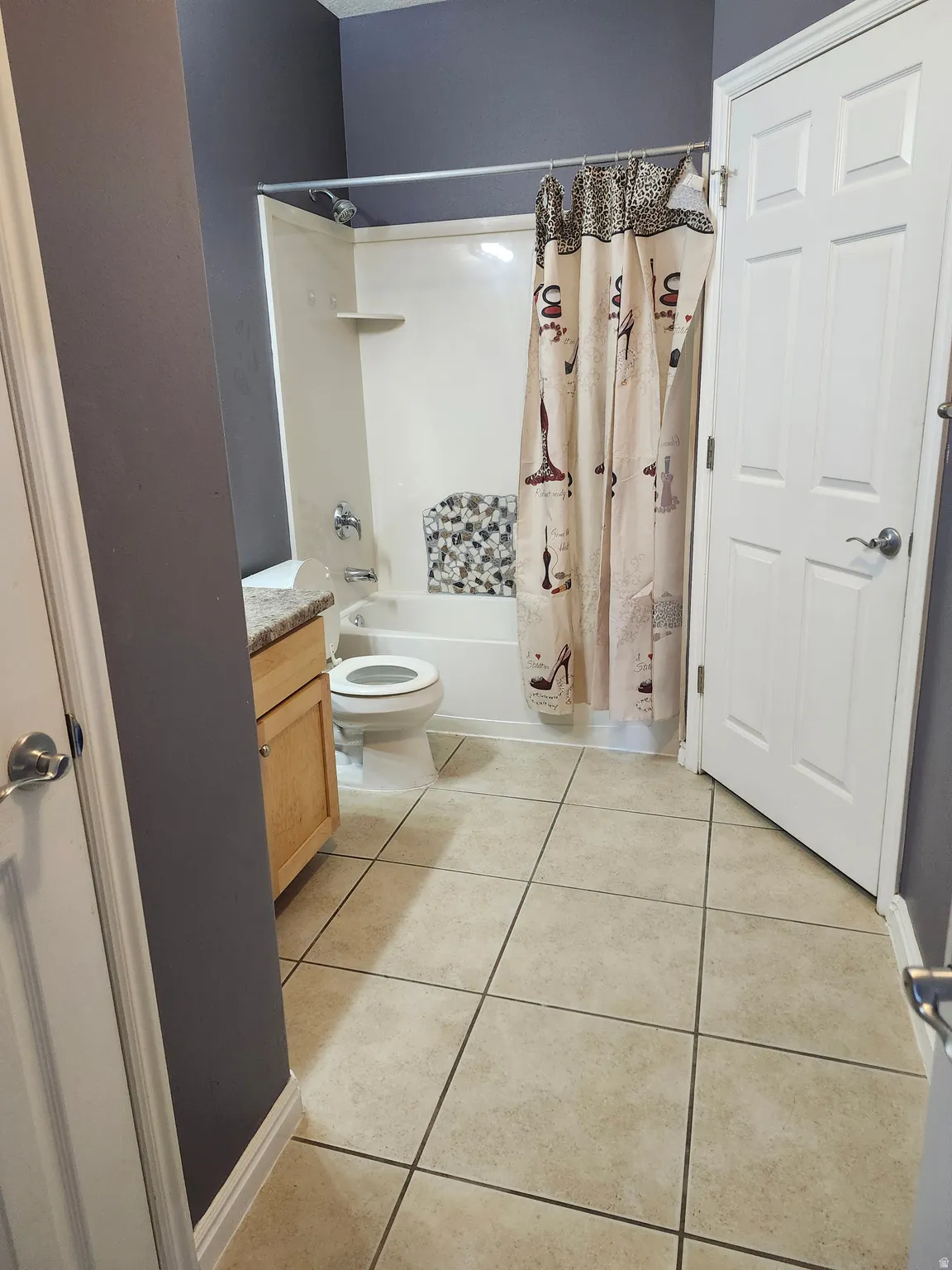 Full bathroom featuring a single-piece tub and shower unit, a light wood-finish vanity with a light-colored countertop, and square tile flooring