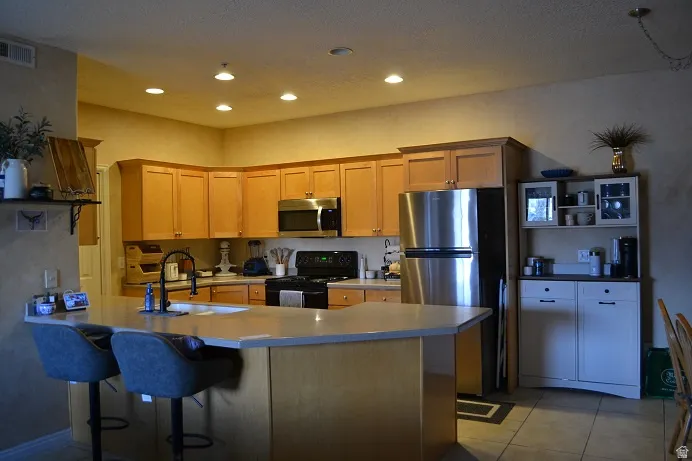 Kitchen with wood cabinetry, stainless steel appliances, recessed ceiling lighting, and a breakfast bar