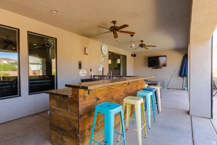 Covered patio featuring a built-in bar with a sink, two ceiling fans, and a wall-mounted television