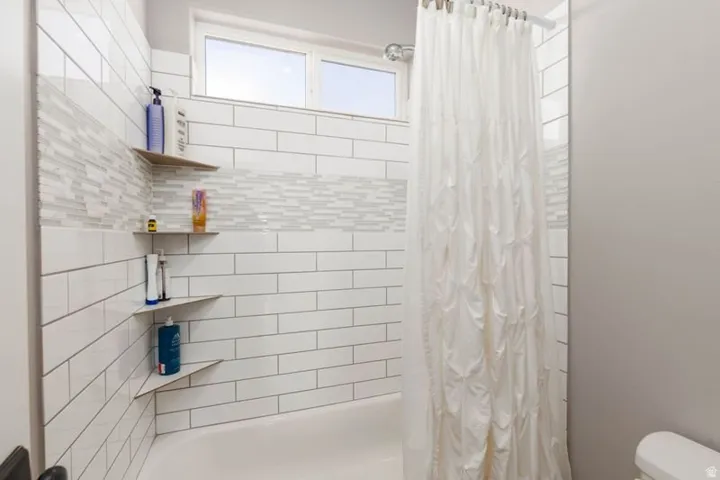 White subway tile surround with a mosaic accent band, integrated corner shelving, and an upper window