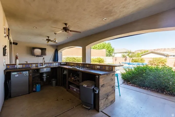 Outdoor kitchen featuring a built-in sink, integrated refrigerator, ceiling fans, and a tiled backsplash