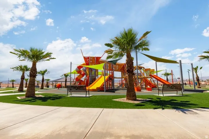 Community playground featuring multiple slides, climbing structures, shade sails, and artificial turf