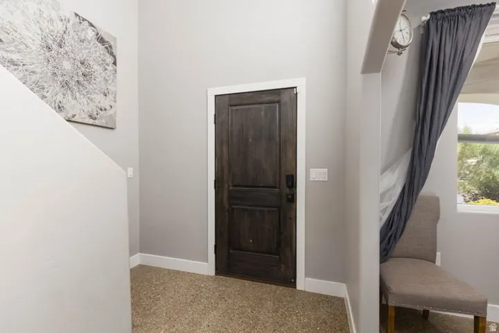 Textured flooring with white baseboards, dark wood door with white trim, and a window with exterior scenery