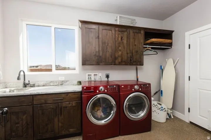 Laundry room featuring a window, wood-finish cabinetry, a utility sink, and stone-finish countertops
