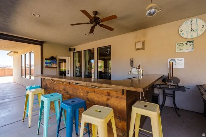 Outdoor entertaining area featuring a built-in bar with a wood-finish countertop, a mounted ceiling fan, recessed lighting, and a built-in sink with a faucet