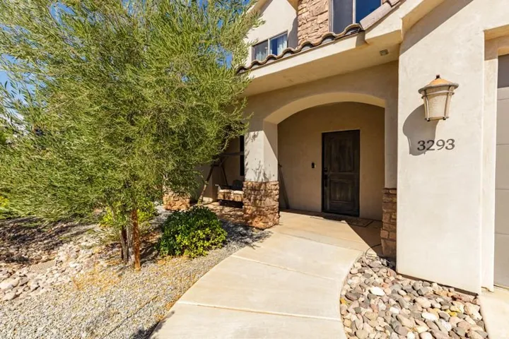 Arched entryway with a textured wood door, stone facade accents, and a decorative exterior light fixture