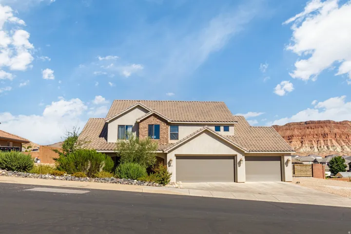 Terracotta tile roof with multi-story stucco and brick facade, attached two-car garage, and desert landscaping