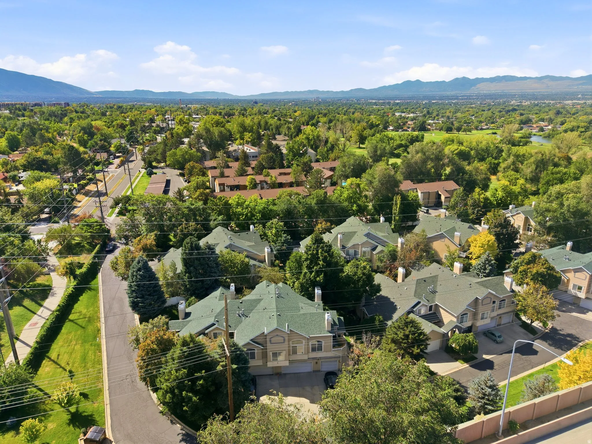 Residential community featuring multiple buildings with green shingle roofs, surrounded by mature trees and landscaping