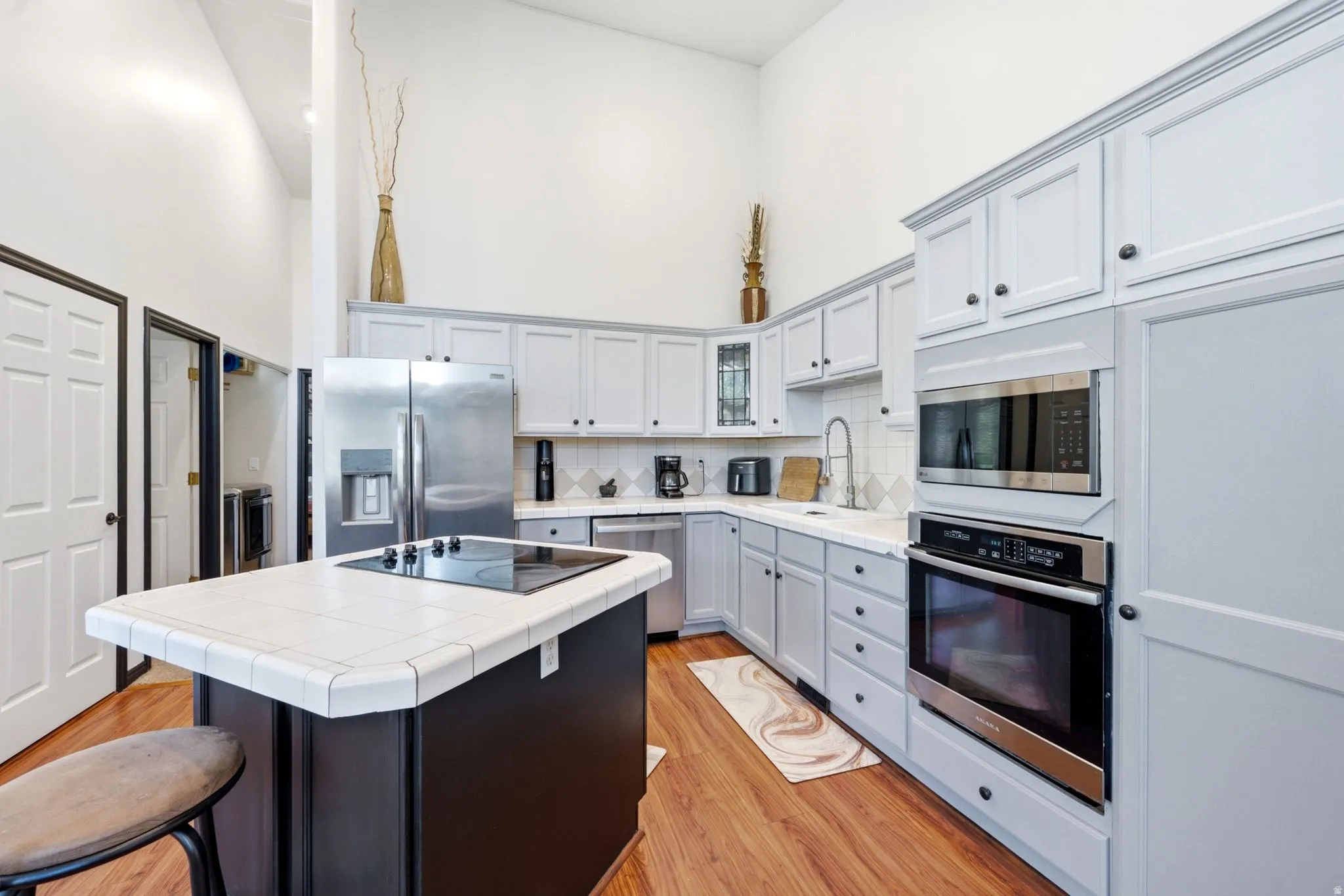Vaulted ceilings complement the kitchen featuring an island with a built-in cooktop, light-toned cabinetry, stainless steel appliances, and wood-finish flooring