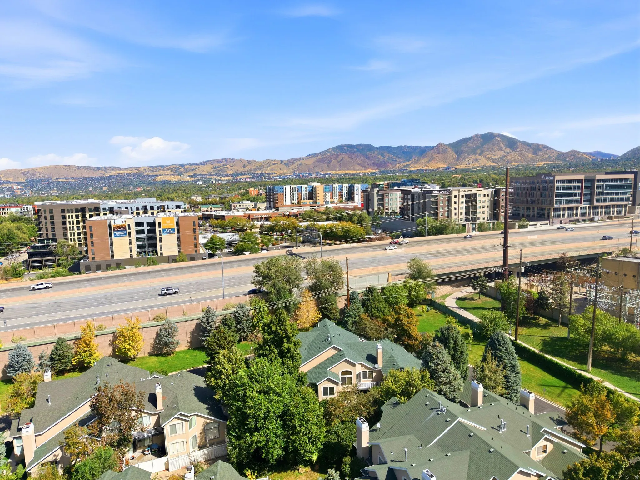 Expansive urban landscape with distant mountains, multiple residential and commercial structures, and a prominent highway